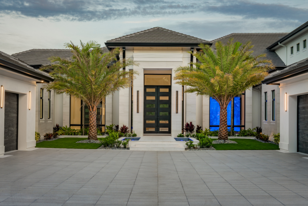 Modern luxury home entrance featuring custom double front doors, stone facade, and palm trees in Naples, FL.