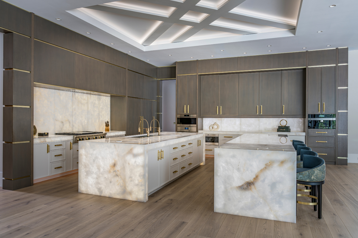 Luxury kitchen design featuring two custom waterfall quartz islands with backlit backsplash, dark wood cabinetry, and gold hardware.
