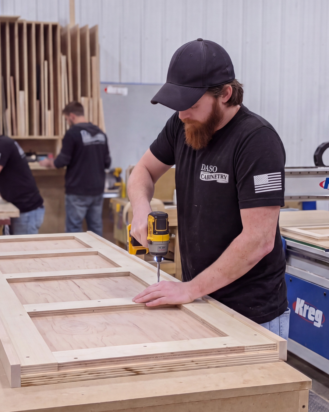 Cabinet maker in a workshop using a power drill to assemble a custom wooden door panel